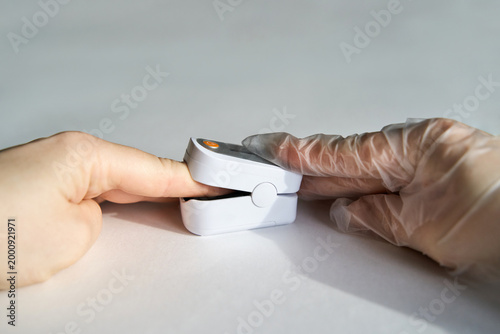 Fingertip Pulse Oximeter On Finger Being Measured By Gloved Hand On White Table Top With Neutral Background In Clinical Setting During Daytime Health Check.