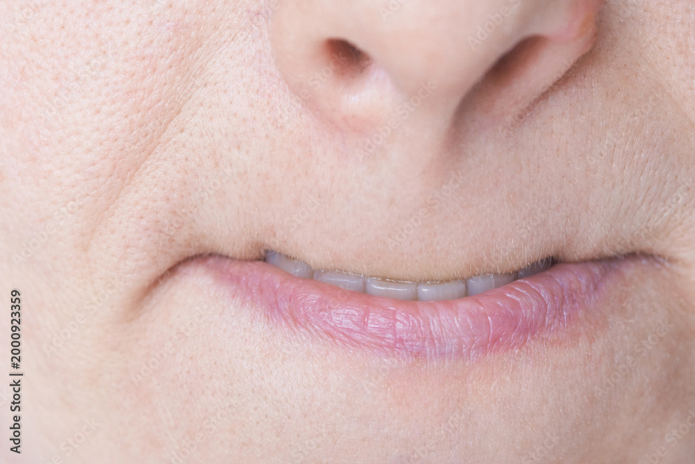 Fototapeta premium Mature Woman Pursing Lips With Slight Smile Showing Teeth In Extreme Close Up Lower Face Portrait Clinical Style Setting Focusing On Mouth Line Skin Texture And Nasolabial Detail.
