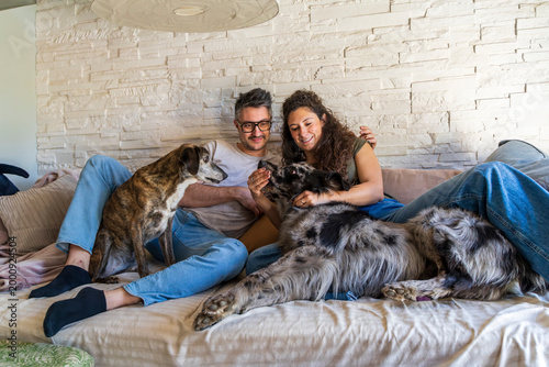 Fotografie Happy couple interacting with their pets while lounging on a sofa at home