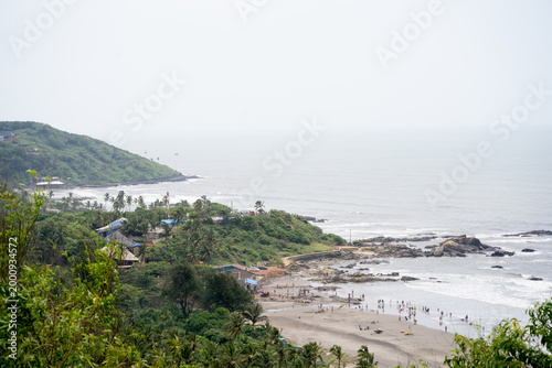 High angle view of Sinquerim Candolim beach in Goa with people enjoying shoreline, rocky coast, and waves during a busy day.