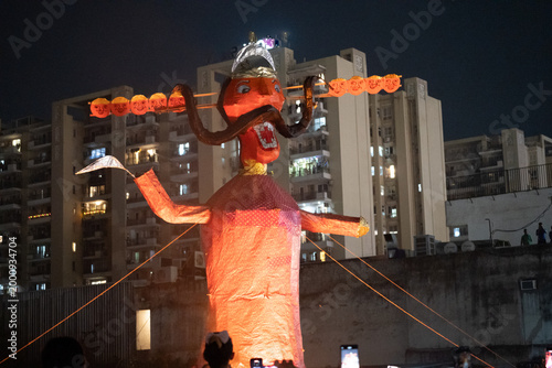 Colorful Ravana effigy with multiple heads on fire during Dussehra festival, set against urban residential buildings at dusk in India.