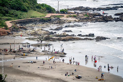 High angle view of Sinquerim Candolim beach in Goa with people enjoying shoreline, rocky coast, and waves during a busy day.