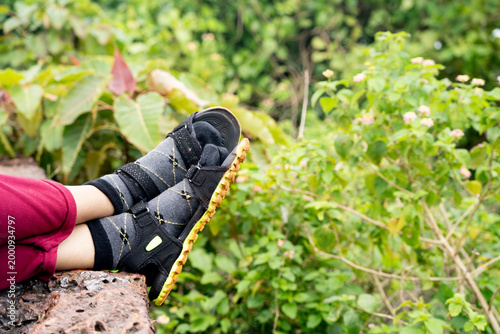 Close-up of person resting legs wearing sandals and socks, set against lush green foliage, conveying relaxation and outdoor leisure vibe.