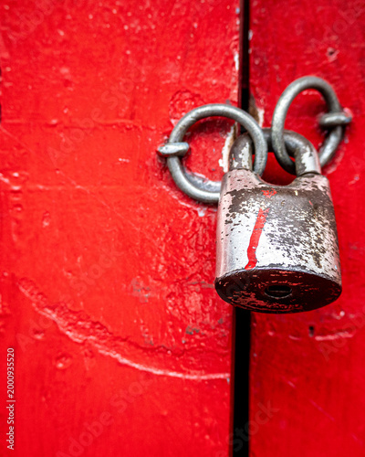 Close up of an old metal padlock securing a vivid red wooden door, symbolizing security, restriction, privacy, and protection concepts.
