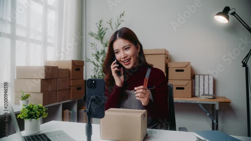 Asian female business owner managing orders and writing address on package for delivery from home office