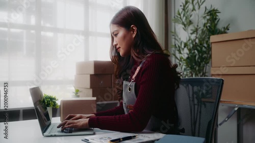 Asian entrepreneur typing on laptop managing online orders for her small business ecommerce startup in her home office