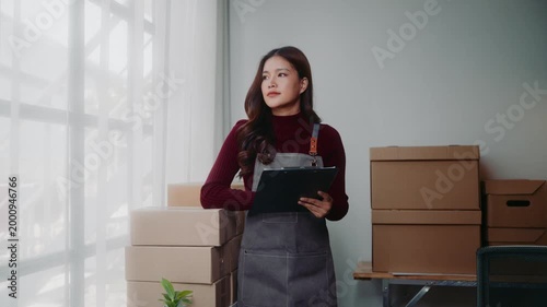 Asian entrepreneur checking inventory and writing on a clipboard in her small business warehouse office