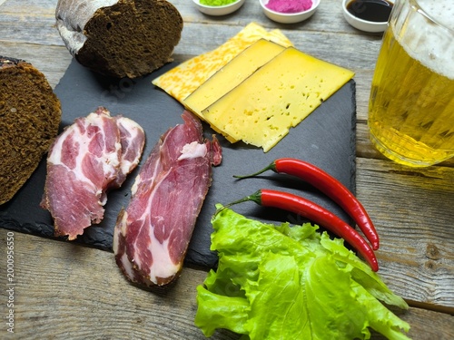 Beer snack on a granite cutting board, with slices of cheese, smoked ham, salad and side dishes laid out on it, and a glass of beer.