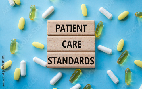 PATIENT CARE STANDARDS symbol. Concept words PATIENT CARE STANDARDS on wooden blocks. Beautiful blue background with pills. Healthcare and PATIENT CARE STANDARDS concept. Copy space.