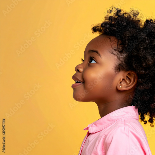 Retrato de niña pequeña sonriendo y mirando hacia arriba sobre fondo amarillo con expresión alegre, concepto de infancia feliz, familia, educación, salud o marcas infantiles con espacio para texto
