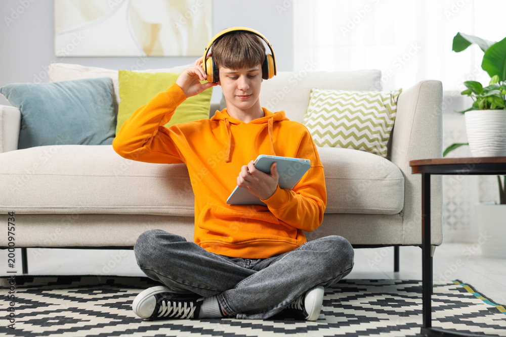 Obraz premium Teenage boy in headphones using tablet on floor at home