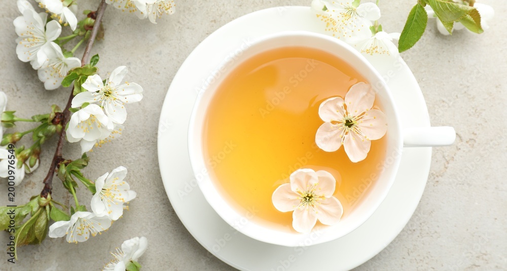 Fototapeta premium Aromatic tea in cup and flowers on light grey table, flat lay