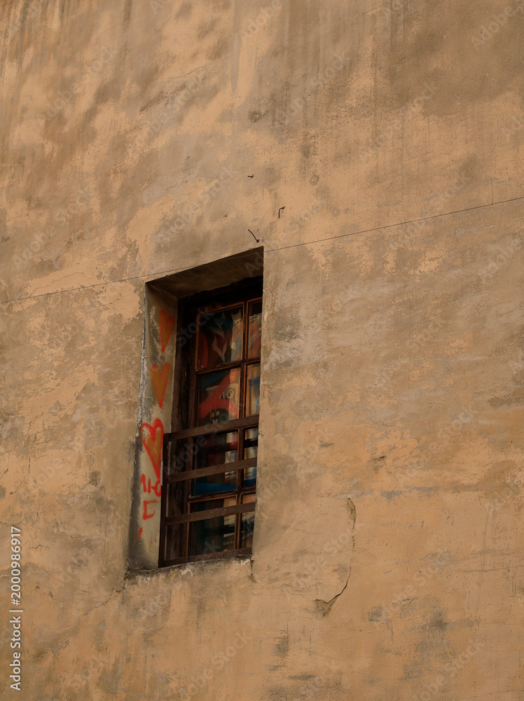 Obraz premium A window with bars, decorated with hearts, on an old wall.