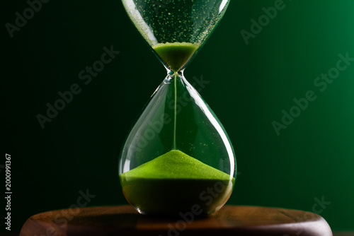 A green hourglass counting down against a green background, representing the concept of working with time and using time most efficiently.