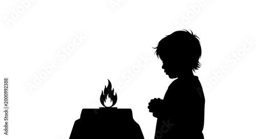 Silhouette of a young child praying before a small flickering candle flame.
