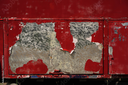 Flaking paint reveals metal on red door.
