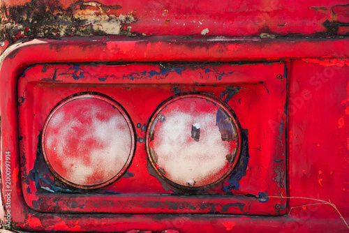A close-up photograph of heavily rusted and weathered dual red tail lights on an old vehicle.