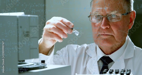 Inspecting scientist holding glass vial at bench with equations on glass, lab coat, tie, copy space