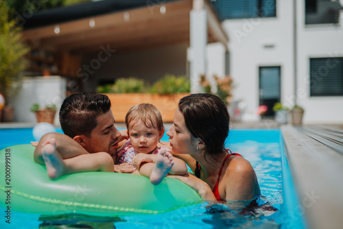 Tableau sur toile Parents and child having fun with floatie in garden swimming pool
