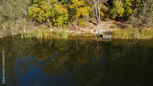 Quadro su tela Lake shore reflecting autumn trees and a small dock