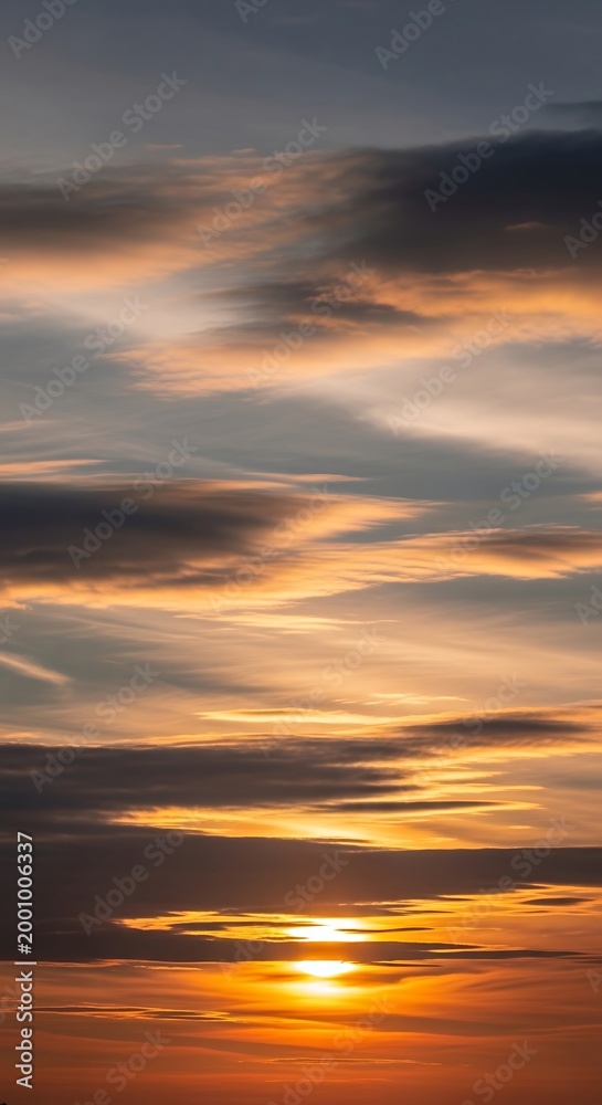 Fototapeta premium Fiery sunset streaks across a cloudy sky, painting the horizon with warm hues