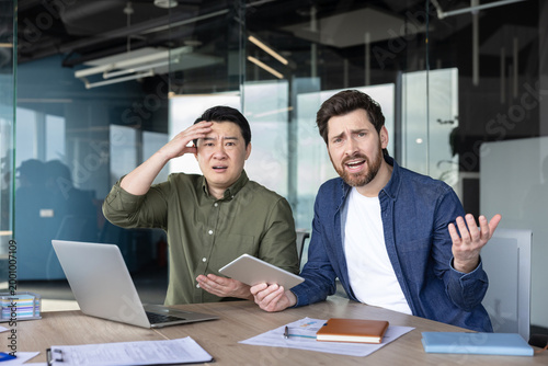 Fotografía Diverse business partners sitting at an office desk, looking shocked and frustra