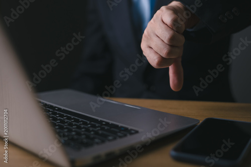 Businessman showing thumb down hand sign in front of a laptop. Concept of business failure, negative feedback, rejected proposal, bad review, and professional disappointment in the office.