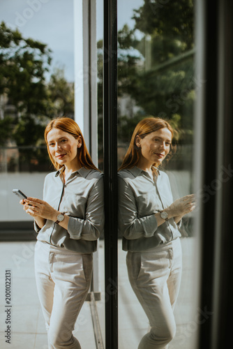 Photos Woman enjoying a moment of reflection while using her smartphone indoors
