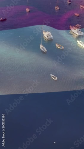 Vertical video: Rising tide driving dark band sliding over moored boats and rippling teal water