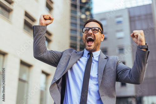 Excited Businessman Celebrating Success With Arms Raised Outside Corporate Office Building