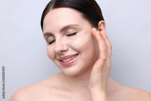 Bild auf Leinwand Beautiful woman with smear of foundation on her face against light background
