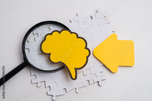 Mental health diagnostics concept with magnifying glass yellow brain silhouette and puzzle pieces on white background