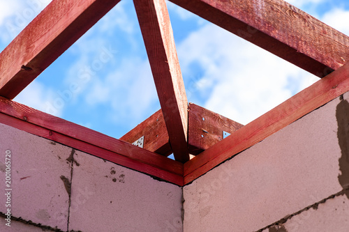 Corner of roof frame with fire-retardant treated wooden beams on unfinished house against blue sky, showing structural joint, protected timber and residential construction process