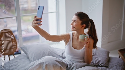 Sensual woman posing mobile phone selfie in morning bed closeup. Modern female