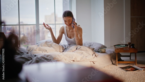 Carefree woman talking cell phone in bedroom. Lady calling smartphone laughing