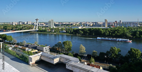 Panoramic Bratislava skyline with SNP UFO Bridge and cruise ship on Danube river in Slovakia. Luxury rooftop terrace view for urban living, property development and investment real estate market.