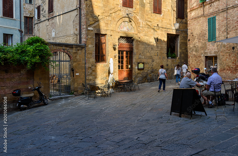 Fototapeta premium Medieval narrow street with tables of restaurant in Siena, Tuscany, Italy. Architecture and landmark of Siena. Cozy cityscape of Siena in Siena, Tuscany, Italy.