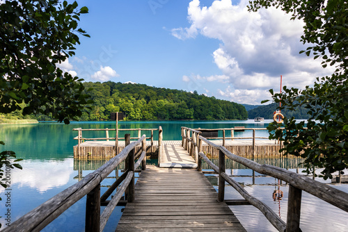 Canvas-taulu Scenic wooden pier clear turquoise lake toward ferry boat passengers green forest Plitvice lakes national park