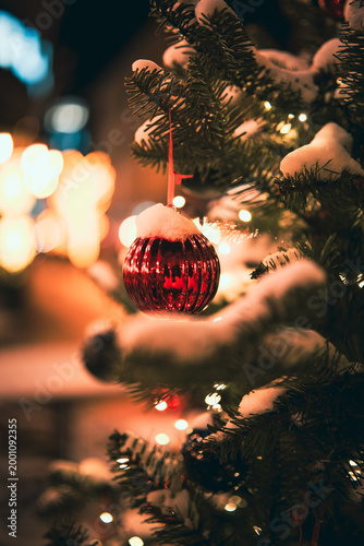 Red Christmas bauble on a snowy fir tree branch with warm bokeh lights