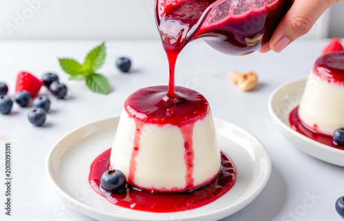 Panna cotta on a plate being drizzled with berry sauce, close up, creamy dessert with glossy topping, elegant food photography.