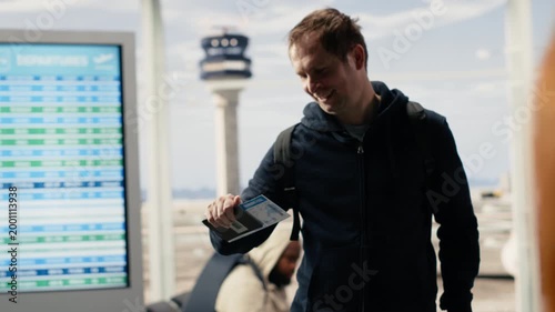 Man traveler verifying boarding pass and passport before flight departure, people with suitcases and carry-on luggage preparing for boarding plane. Authentic air travel and airline industry.