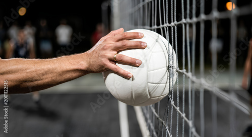 Close-up of a volleyball player hand gripping the ball against the net during an intense indoor match or training session.
