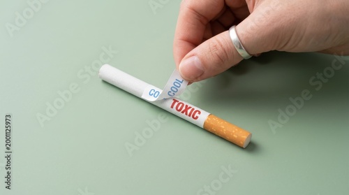 A hand holds a cigarette with a toxic label on a table.
