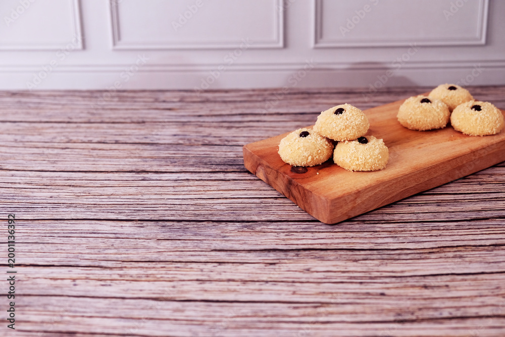 Fototapeta premium Kue Monde Susu or cookies rest on a rustic wooden board. Each cookie has a small choco chip on top. The board rests on weathered wood, adding warmth to the scene. Ideal for cozy cafe or home baking 