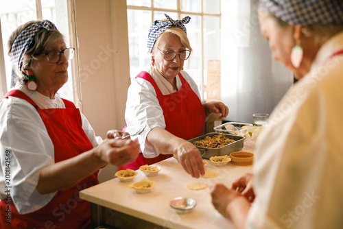Senior Caucasian women actively engaged in preparing traditional pastries, showcasing ageless vitality under natural soft light.