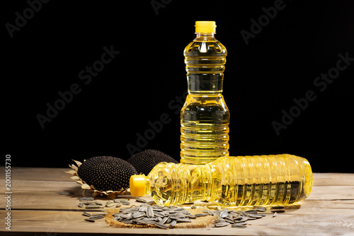 A bottle of pure golden sunflower oil placed on a rustic wooden table with seeds and dried sunflowers, isolated on a dark black background for copy space.