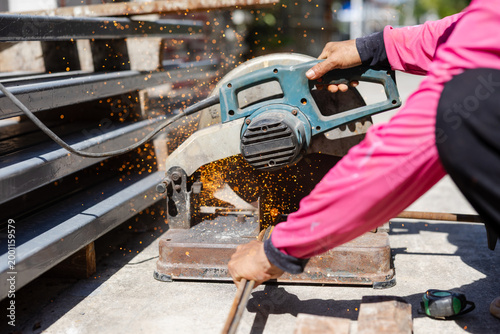 Worker in pink shirt using angle grinder cutting metal with flying sparks