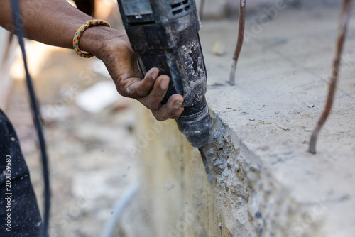 Construction worker using rotary hammer drill to break concrete wall