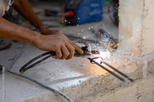 Welder using welding tongs on rebar with bright sparks and smoke