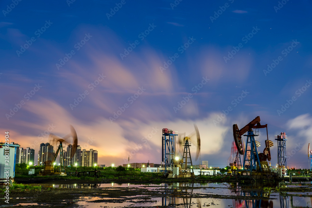Fototapeta premium in the evening, oil pumps are running, The oil pump and the beautiful sunset reflected in the water, the silhouette of the beam pumping unit in the evening.